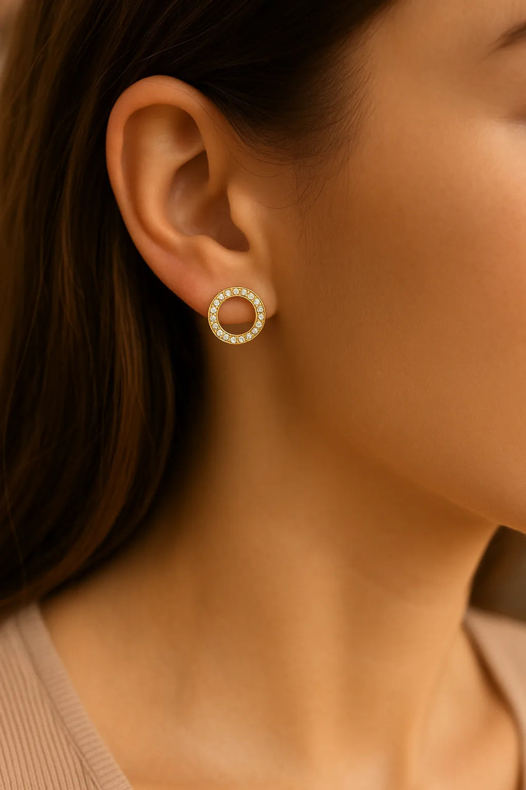 Vergoldeter runder Ohrstecker mit klar funkelnden Zirkonia-Steinen, getragen am Ohr einer Frau; eleganter, zeitloser Kreis-Ohrring im minimalistischen Stil.