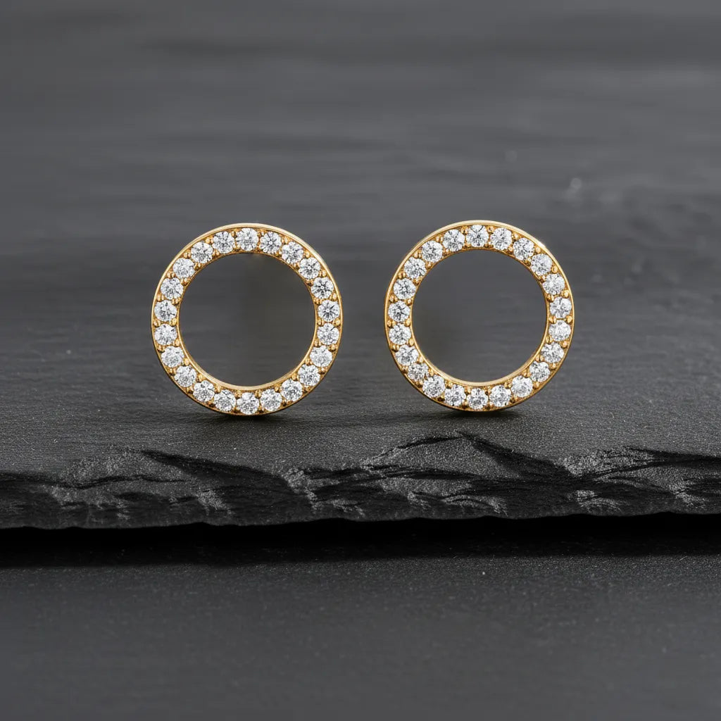 Runde vergoldete Damen Ohrstecker in offener Kreisform, komplett mit klar funkelnden Zirkonia besetzt, elegant inszeniert auf dunklem Schieferhintergrund.
