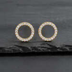 Runde vergoldete Damen Ohrstecker in offener Kreisform, komplett mit klar funkelnden Zirkonia besetzt, elegant inszeniert auf dunklem Schieferhintergrund.