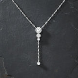 "Silberne Y-Kette mit drei funkelnden Zirkonia-Steinen in Krappenfassung, herunterhängender Kette und einem weiteren Zirkonia-Stein am Ende, präsentiert auf dunklem, kontrastierendem Schieferhintergrund. Elegante Damenhalskette mit Anhänger, perfekt für einen modernen, schlichten Look."