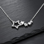 Damen Halskette aus 925 Sterling Silber mit mehreren zusammenhängenden Sternanhängern, teils pavé mit klaren Zirkonia besetzt, edel präsentiert auf dunklem Schieferhintergrund.