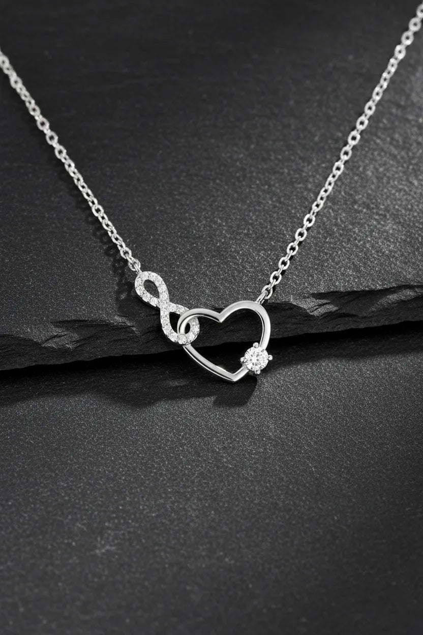 Feine Damen Halskette aus 925 Sterling Silber mit Herz-und-Unendlichkeitsanhänger, besetzt mit funkelnden Zirkonia und rundem Solitärstein, edel inszeniert auf schwarzem Schiefer.