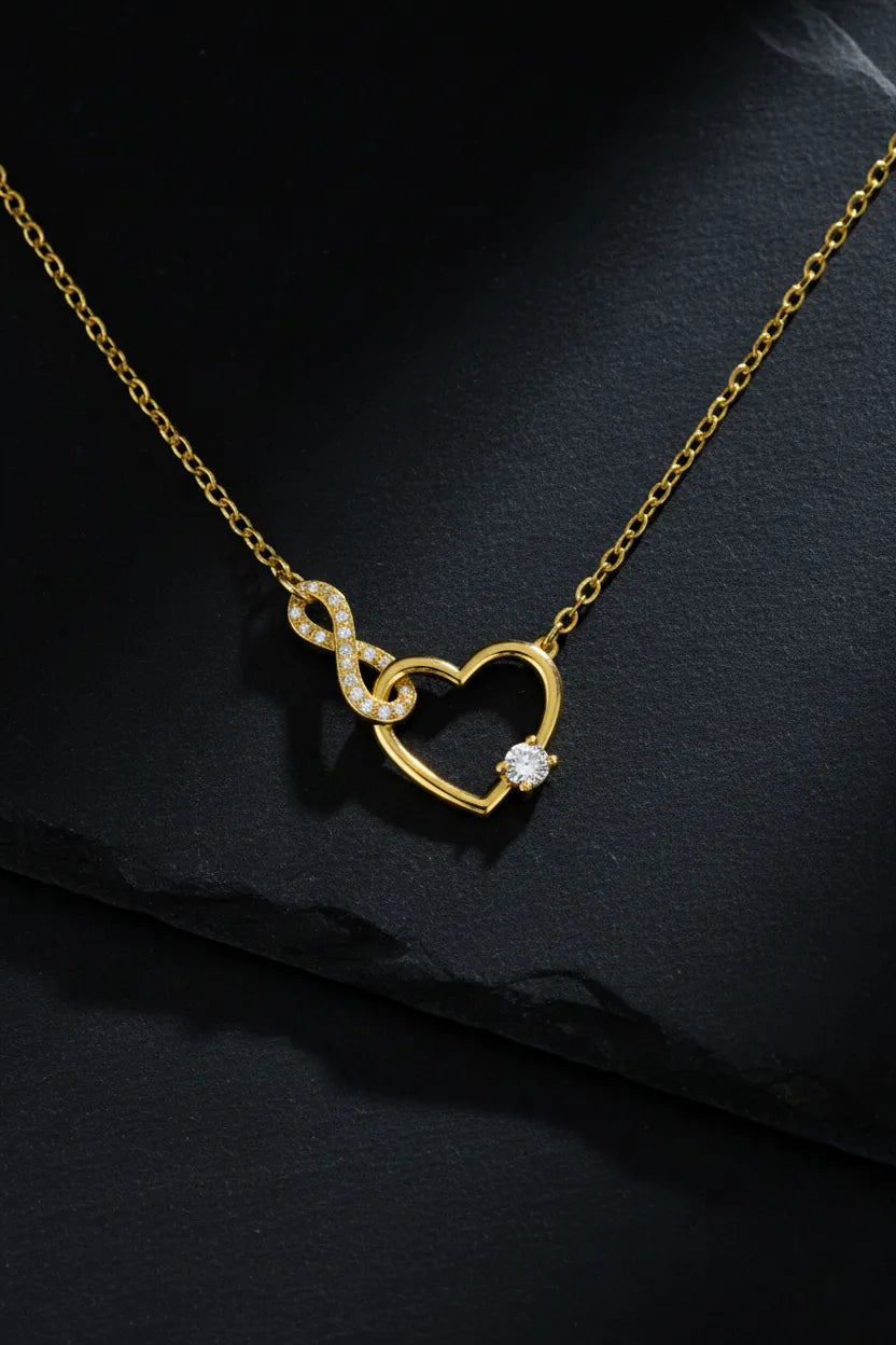 Vergoldete Damen Halskette mit offenem Herz- und Infinity-Anhänger, besetzt mit klar funkelnden Zirkonia und rundem Solitärstein, edel präsentiert auf dunklem Schieferhintergrund.
