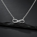 Feine Damen Halskette aus 925 Sterling Silber mit Infinity-Anhänger, teilweise besetzt mit klar funkelnden Zirkonia-Steinen, edel präsentiert auf schwarzem Stein-Hintergrund.