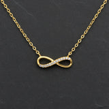 Vergoldete Damen Halskette mit filigranem Infinity-Anhänger, teilweise besetzt mit klar funkelnden Zirkonia-Steinen, elegant präsentiert auf dunklem Schieferhintergrund.