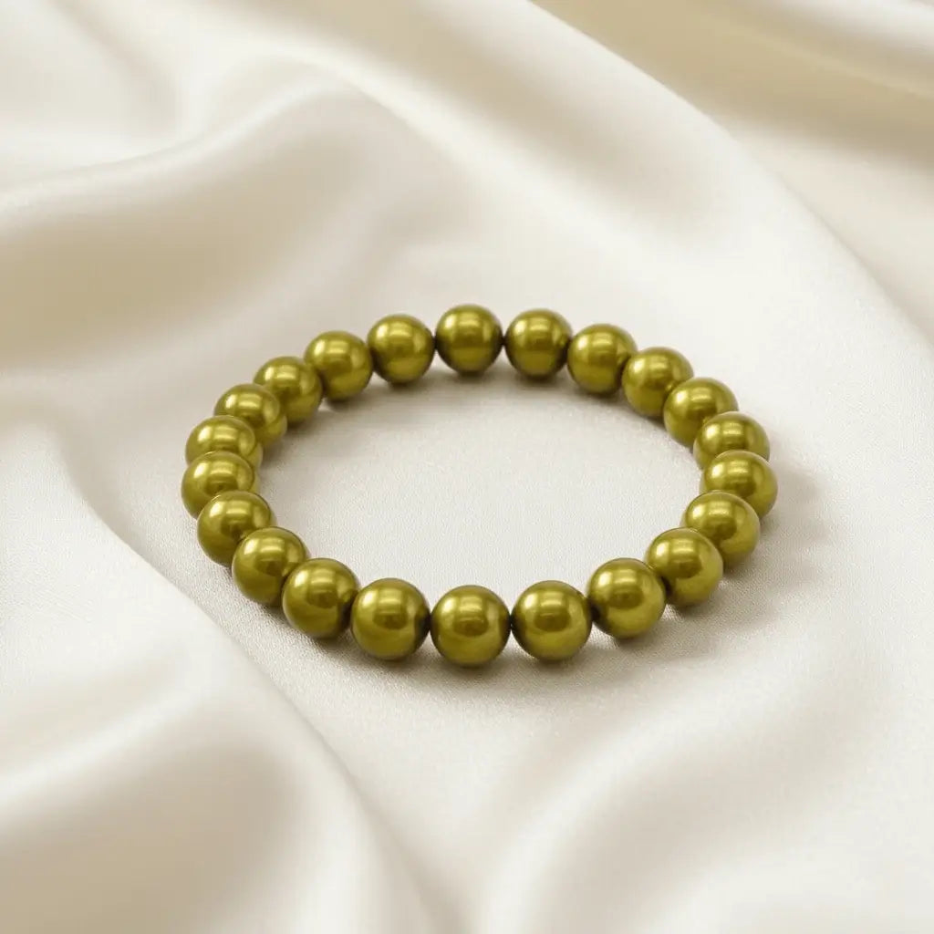Ein Armbands aus glänzenden, olivgrünen Perlen, das auf einem beigefarbenen, seidenartigen Stoff liegt.