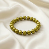 Ein Armbands aus glänzenden, olivgrünen Perlen, das auf einem beigefarbenen, seidenartigen Stoff liegt.