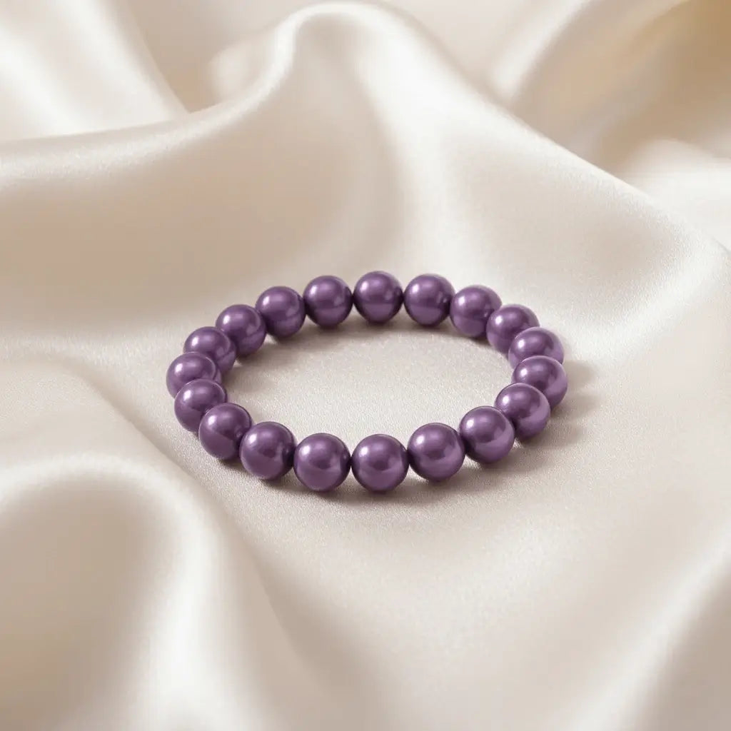 Ein Armbands aus glänzenden, lila Perlen, das auf einem beigefarbenen, seidenartigen Stoff liegt.