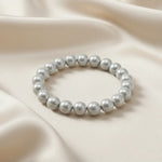 Ein Armbands aus glänzenden, silberfarbenen Perlen, das auf einem beigefarbenen, seidenartigen Stoff liegt.