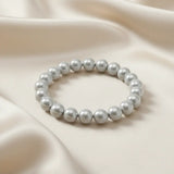 Ein Armbands aus glänzenden, silberfarbenen Perlen, das auf einem beigefarbenen, seidenartigen Stoff liegt.