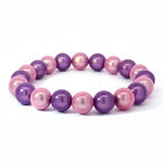 Ein elegantes Armband aus glänzenden rosa und violetten Perlen, gleichmäßig aufgereiht auf einem elastischen Band. Die Perlen schimmern im Tageslicht und zeigen einen sanften Farbverlauf zwischen zartem Rosa und kräftigem Violett.