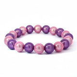Ein elegantes Armband aus glänzenden rosa und violetten Perlen, gleichmäßig aufgereiht auf einem elastischen Band. Die Perlen schimmern im Tageslicht und zeigen einen sanften Farbverlauf zwischen zartem Rosa und kräftigem Violett.
