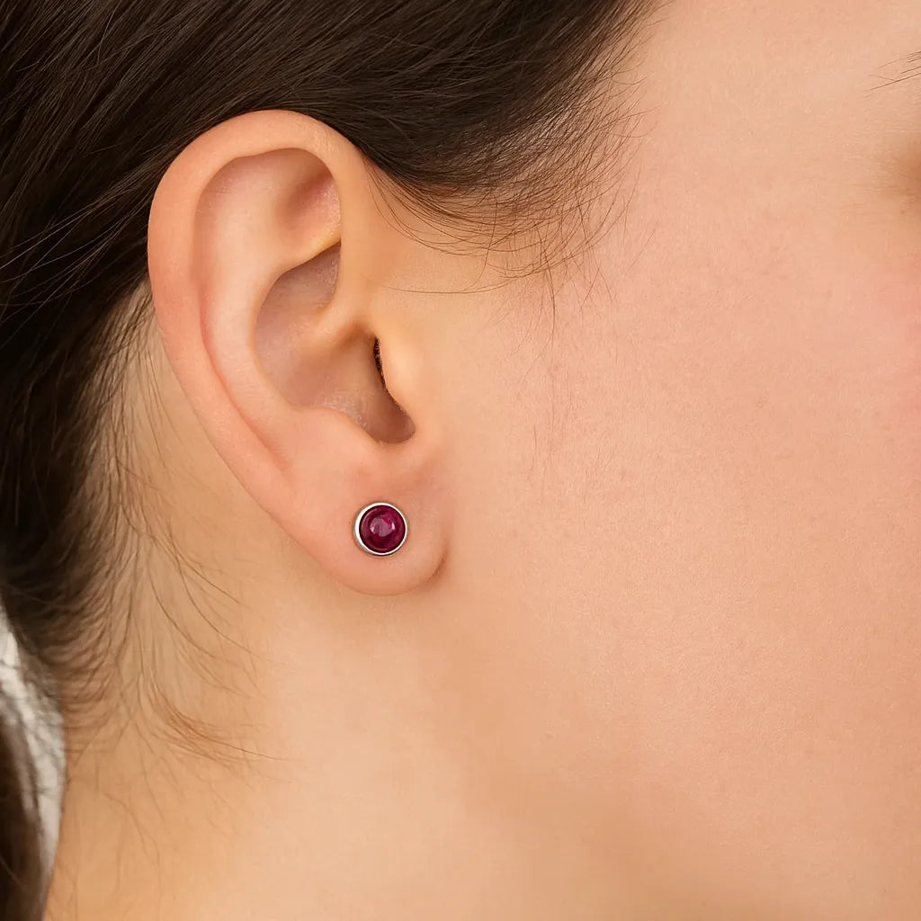 Nahaufnahme eines Ohrs mit einem eleganten Ohrstecker aus 925er Silber und rundem, tiefrotem Granat-Cabochon. Der Ohrstecker wirkt edel und dezent zugleich.