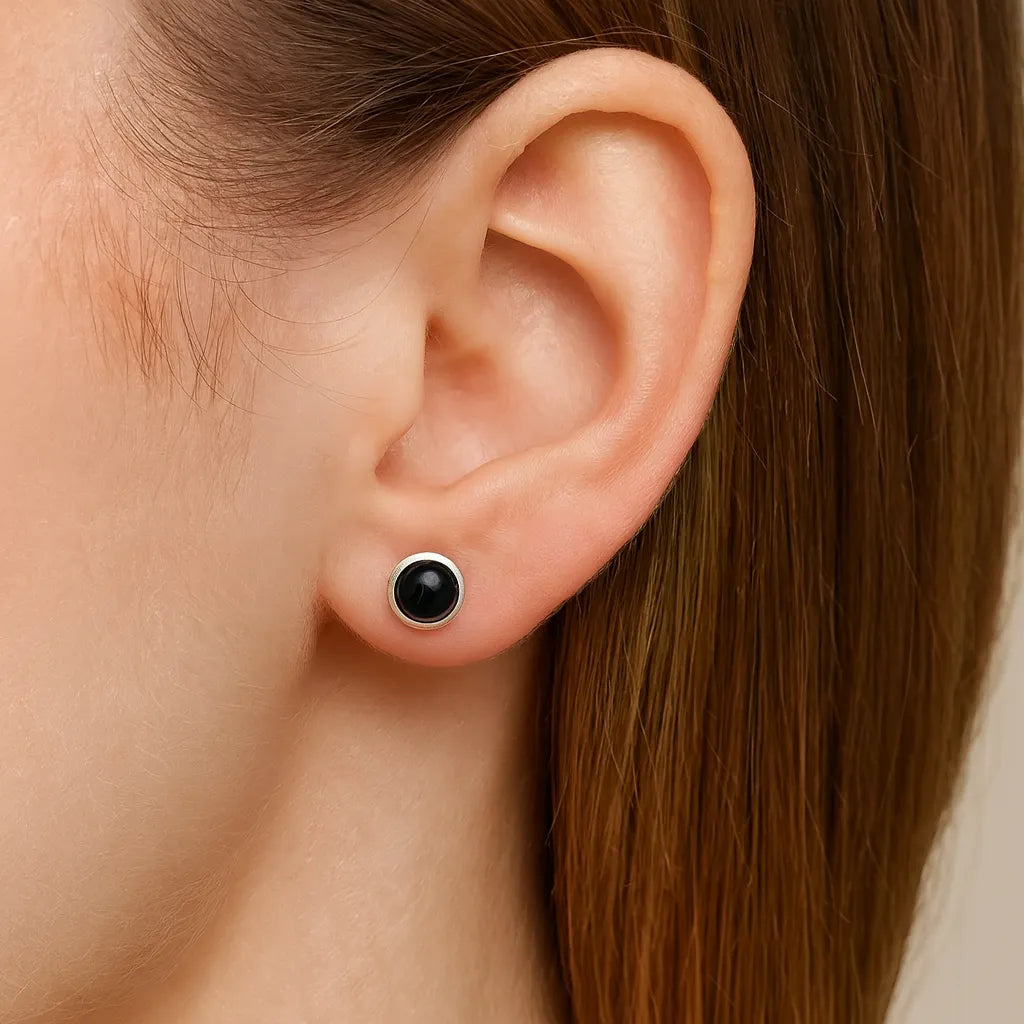 Eine Frau trägt einen eleganten Ohrstecker aus 925er Sterlingsilber mit rundem, schwarzem Onyx-Cabochon. Der glänzende Stein sitzt mittig im silbernen Rahmen und schmiegt sich dezent ans Ohr – ein stilvoller, klassischer Look für jeden Anlass.