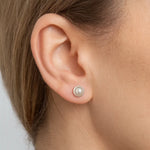 Nahaufnahme eines weiblichen Ohrs mit einem eleganten Ohrstecker aus 925er Sterlingsilber, besetzt mit einer weißen Perle in glatter Cabochon-Fassung. Der Ohrstecker wirkt klassisch und dezent und verleiht dem Look eine zeitlose, edle Note.