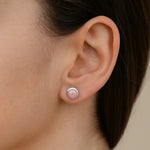 Frau trägt einen Ohrstecker aus 925er Sterlingsilber mit rundem, zart roséfarbenem Rosenquarz-Cabochon. Der elegante Ohrring sitzt dezent am Ohrläppchen und unterstreicht einen femininen, zeitlosen Look.