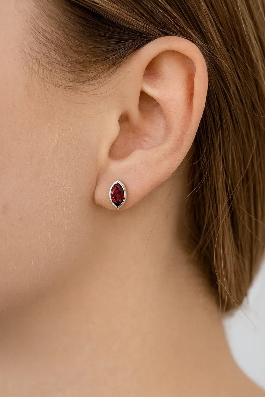 Nahaufnahme eines Ohrs mit einem eleganten Ohrstecker aus Sterlingsilber, besetzt mit einem marquisförmigen, tiefroten Granatstein in glänzender Fassung. Der Schmuck verleiht dem Look eine edle und zugleich moderne Note.