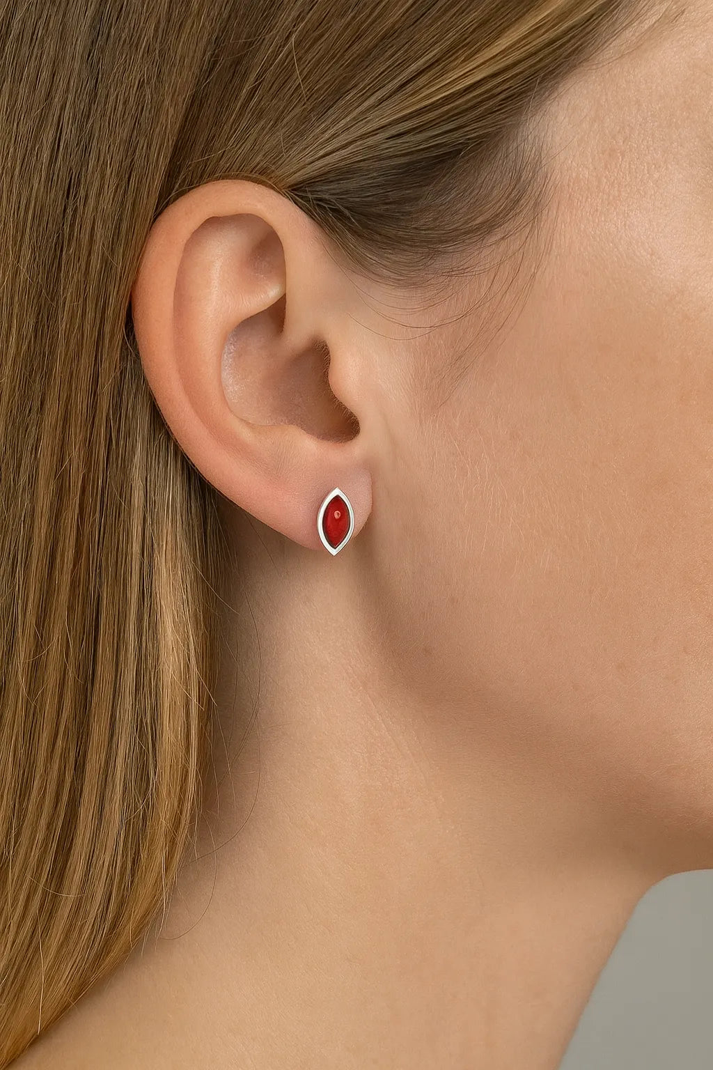 Nahaufnahme eines Ohrs mit einem eleganten Ohrstecker aus 925er Sterlingsilber und rotem Korallen-Cabochon in Marquiseform. Der Ohrstecker schimmert dezent und wirkt als stilvoller Farbakzent auf der Haut.