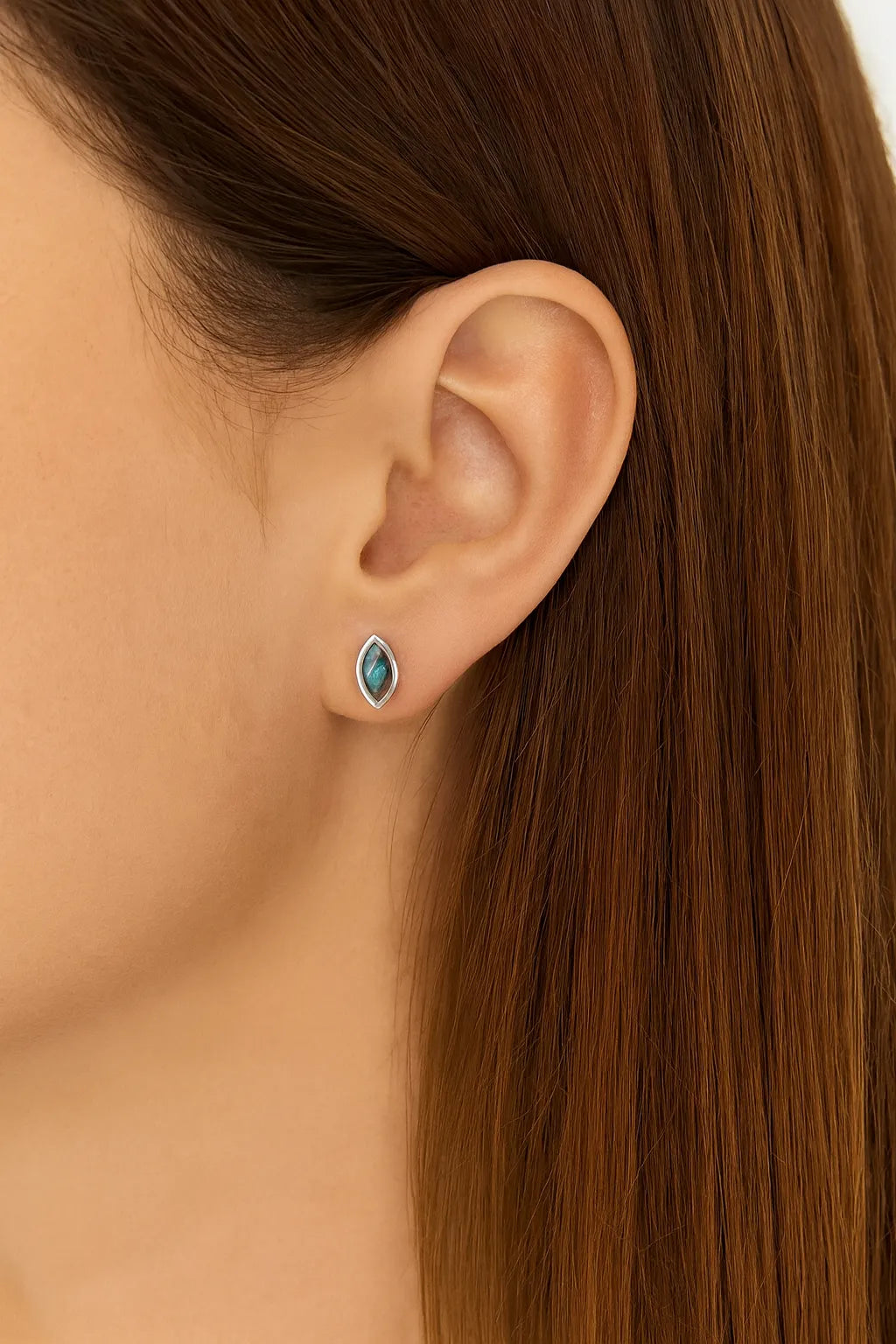 Nahaufnahme eines Ohres mit einem eleganten Ohrstecker in Marquiseform aus 925er Sterlingsilber, gefasst mit einem schimmernden Labradorit-Cabochon, der in Blau- und Grautönen irisierend leuchtet. Der Ohrstecker wirkt dezent und edel am Ohr getragen.