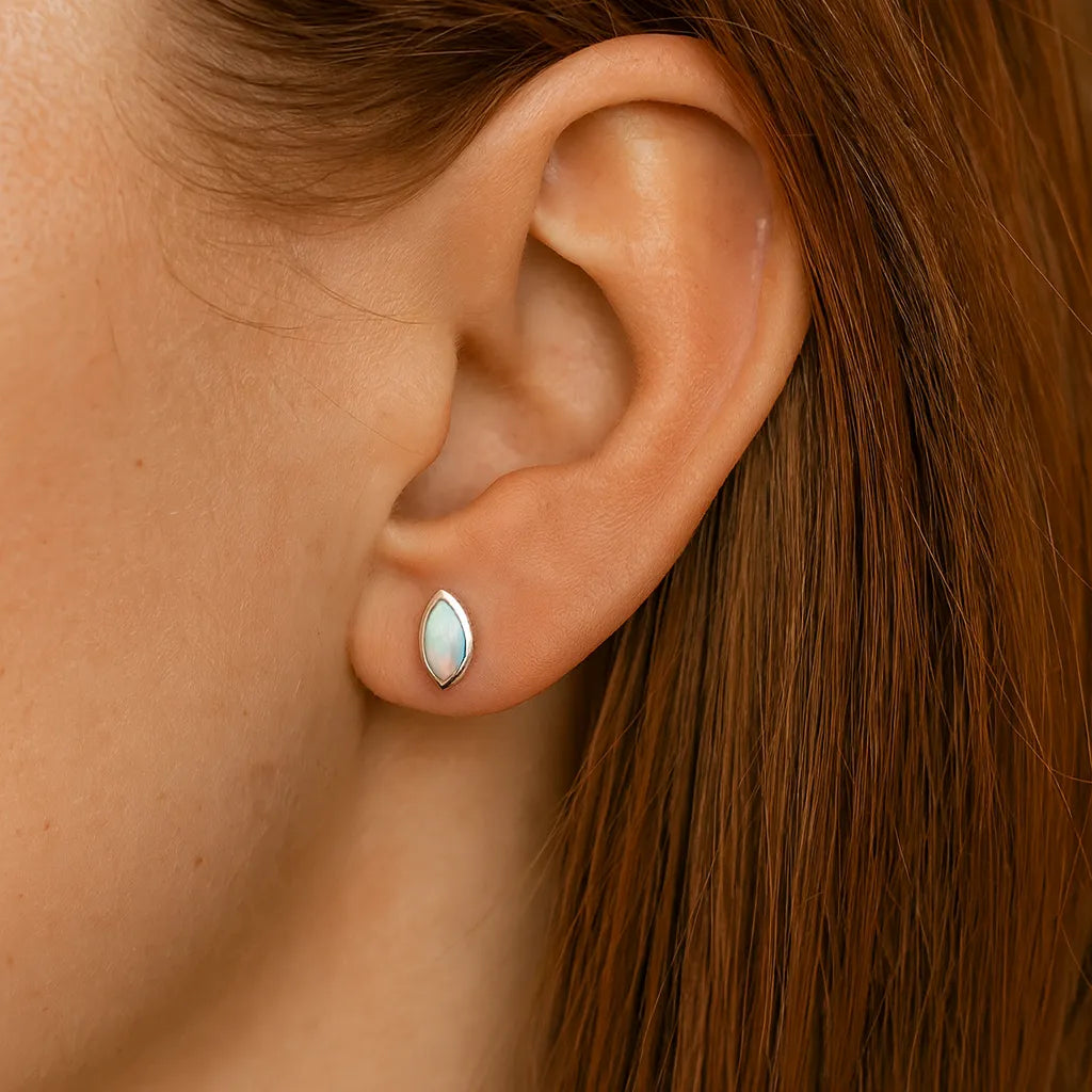 Nahaufnahme einer Frau in Seitenansicht mit einem kleinen, marquiseförmigen Ohrstecker aus Silber und schimmerndem Opal. Der etwa 5 mm lange Ohrring sitzt dezent am Ohrläppchen, während Haut und Haar in warmem, natürlichem Licht erscheinen.