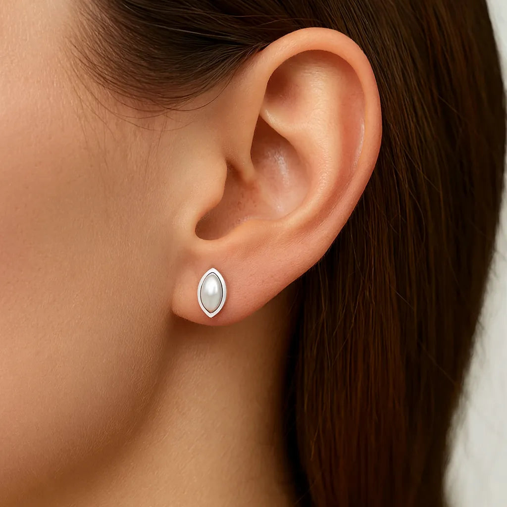 Nahaufnahme eines Ohrs mit einem eleganten Ohrstecker in Marquiseform aus 925er Sterlingsilber, besetzt mit einer schimmernden weißen Perle im Cabochonschliff. Der Ohrstecker verleiht dem Look eine klassische, feminine Note.