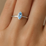 Ein eleganter Damenring aus poliertem 925er Sterlingsilber mit einem 5 mm langen, facettierten blauen Topas im Navette-Schliff. Der Ring ist an der Hand einer Frau am Ringfinger zu sehen. Der Fokus liegt auf dem hellblau funkelnden Edelstein, der von einer schlichten, glänzenden Ringschiene gehalten wird.