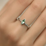 Eine Nahaufnahme einer Frauenhand mit einem filigranen Silberring am Ringfinger. Der Ring zeigt einen zarten, marquiseförmigen Grünquarz von etwa 5 mm Länge in einer glatten Fassung. Der Fokus liegt klar auf dem Ring und dem hellgrün schimmernden Stein, während der Hintergrund weich und neutral bleibt.