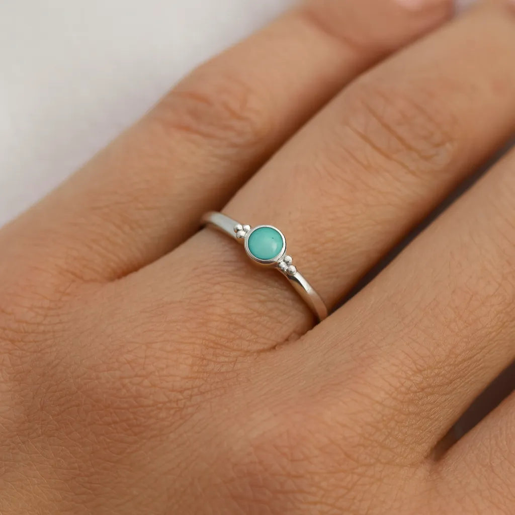 Nahaufnahme einer Frauenhand, die einen eleganten Silberring mit einem rund geschliffenen, hellblauen Aqua-Chalcedon-Cabochon trägt. Der Ring sitzt am Ringfinger, und der Fokus liegt klar auf dem glänzenden Stein, der dezent in einem modernen, minimalistischen Design gefasst ist. Der Hintergrund ist neutral und weich, wodurch der Ring besonders hervorsticht.