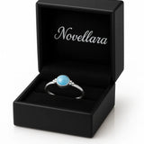 Eleganter Damenring aus Sterling Silber mit rundem blauem Chalcedon Cabochon (4 mm) in Zargenfassung, präsentiert in geöffneter schwarzer Schmuckbox mit Novellara Logo – hochwertiger Silberring mit hellblauem Edelstein als Geschenkidee für Frauen.