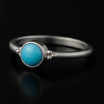 Damenring aus Sterling Silber mit rundem blauem Chalcedon Cabochon (4 mm) in Zargenfassung – filigraner Silberring mit hellblauem Edelstein, edel inszeniert auf schwarzem Hintergrund mit Spiegelung.