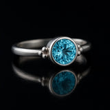 Sterlingsilber-Ring mit brillant geschliffenem blauem Topas, seitliche Ansicht auf schwarzem kontrastreichen Spiegel-Untergrund, professionelle Schmuckfotografie für Produktdarstellung.