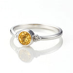 "Feiner Damenring aus Sterlingsilber mit goldgelbem Citrin als Mittelstein, seitlich fotografiert auf hellem reflektierendem Hintergrund mit Spiegelung, hochwertiges Schmuck-Produktfoto für Citrinring."