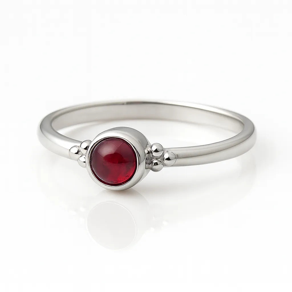 Feiner Damenring aus 925 Sterling Silber mit rundem Granat-Cabochon in tiefem Rot, eingefasst in einer Zargenfassung mit Silberkügelchen-Details, hochwertig fotografiert auf weißem spiegelnden Hintergrund als eleganter Edelsteinschmuck.