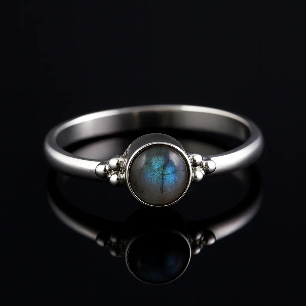 Damenring aus Sterling Silber mit rundem Labradorit Cabochon (4 mm) in Zargenfassung – feiner Silberring mit schimmernd blau-grauem Edelstein, edel präsentiert auf schwarzem spiegelnden Hintergrund.