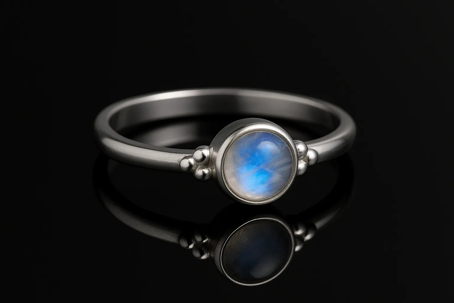 Edler Silberring mit schimmerndem blau-weißem Mondstein, liegend auf schwarzem spiegelndem Hintergrund mit starker Reflexion, hochwertiges Schmuck-Produktfoto seitlich aufgenommen.