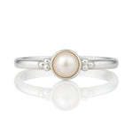 Feiner Damenring aus 925 Silber mit runder Perle und dekorativen Silberkügelchen, liegend auf glänzend weißem Untergrund mit klarer Spiegelung, hochwertiges Schmuckprodukt in Nahaufnahme.