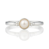 Feiner Damenring aus 925 Silber mit runder Perle und dekorativen Silberkügelchen, liegend auf glänzend weißem Untergrund mit klarer Spiegelung, hochwertiges Schmuckprodukt in Nahaufnahme.