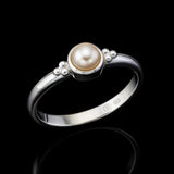 Eleganter 925-Silberring mit champagnerfarbener Perle in runder Fassung, seitliche Nahaufnahme auf schwarzem hochglänzendem Spiegeluntergrund mit starker Reflexion, edler Perlenschmuck für Damen