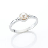 Eleganter Silberring mit runder Creme-Perle in Zargenfassung, seitlich fotografiert auf hellem spiegelnden Untergrund mit weicher Reflexion, filigrane Silberkügelchen als Detail am Ringkopf