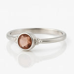 Damenring aus Sterling Silber mit rundem facettierten Rauchquarz in Zargenfassung – filigraner Silberring mit braunem Edelstein auf weißem spiegelnden Hintergrund, eleganter Schmuck für Frauen.