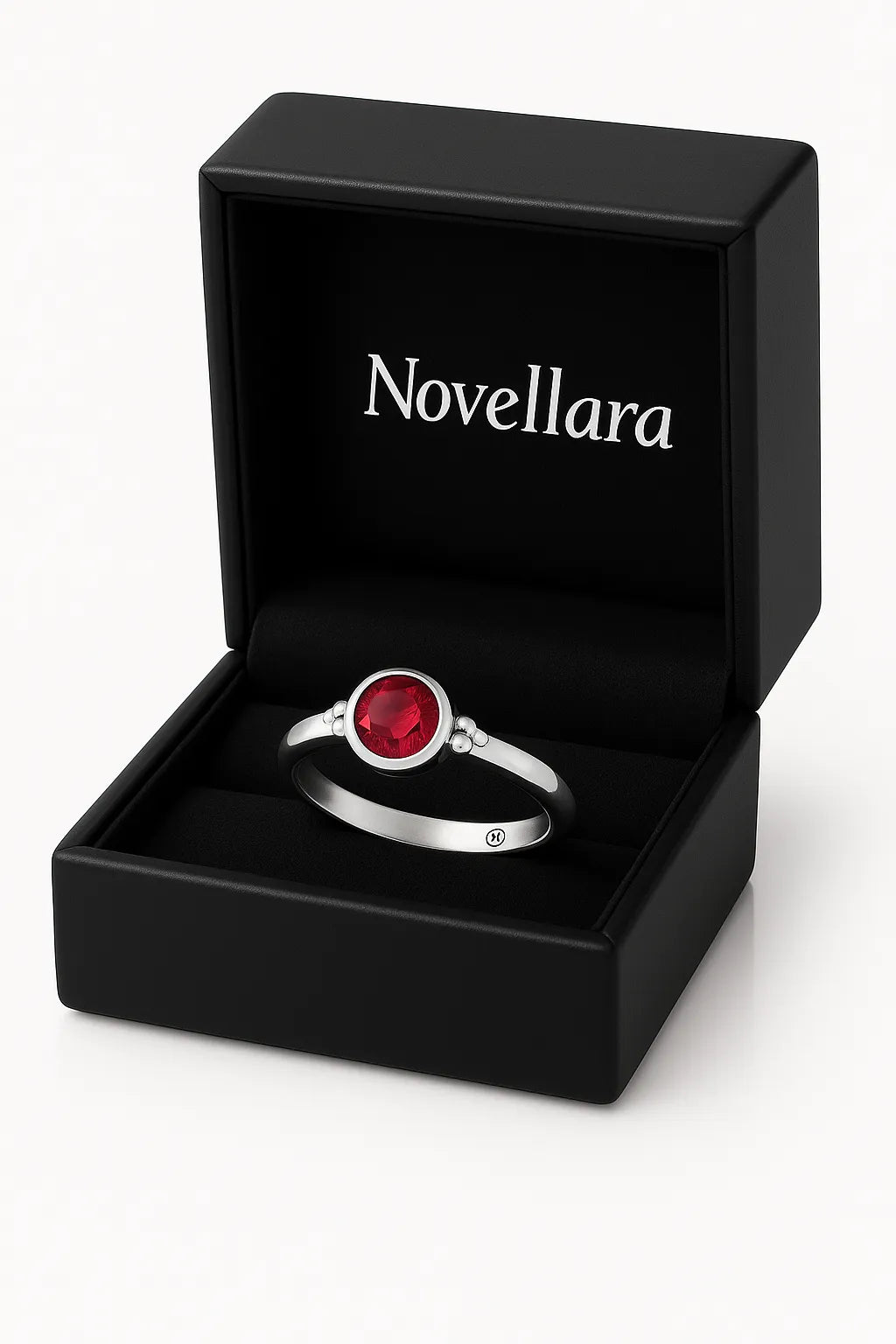 Ein silberner Ring mit einem runden, roten 4-mm-Stein liegt in einer geöffneten schwarzen Schmuckschatulle mit samtiger Einlage. Auf der Innenseite des Deckels steht das Logo „Novellara“ in heller Schrift. Das Bild ist in Studioqualität vor hellem Hintergrund aufgenommen.