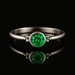 Damenring aus Sterling Silber mit rundem facettierten Smaragd in Zargenfassung – frontale Katalogansicht auf schwarzem spiegelnden Hintergrund, eleganter Silberring mit grünem Edelstein und feinen Silberkügelchen als edles Schmuckstück für Frauen.