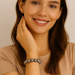 Junge Frau mit schulterlangen braunen Haaren trägt ein elastisches Armband aus silbergrauen Perlen am Handgelenk