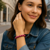 Eine junge Frau in urbaner Umgebung trägt ein pinkfarbenes Perlenarmband am Handgelenk. Der Fokus liegt auf dem Schmuckstück, während die Frau entspannt und stilvoll wirkt.