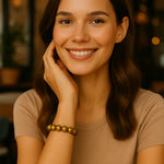 Eine junge Frau sitzt freundlich lächelnd in einem Café. Sie trägt ein goldenes Perlenarmband am Handgelenk, das elegant zur natürlichen Atmosphäre passt.