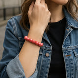 Eine junge Frau trägt ein lachsfarbenes Perlenarmband am Handgelenk. Sie steht in urbaner Umgebung, trägt eine Jeansjacke über einem schwarzen Shirt. Der Fokus liegt auf dem Armband.