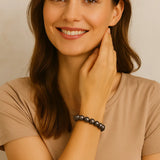 Junge Frau mit braunen Haaren trägt ein elastisches Armband aus dunkelgrauen Perlen am Handgelenk