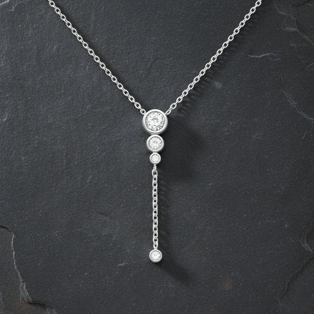 "Silberne Y-Kette mit drei funkelnden Zirkonia-Steinen in Krappenfassung, herunterhängender Kette und einem weiteren Zirkonia-Stein am Ende, präsentiert auf dunklem, kontrastierendem Schieferhintergrund. Elegante Damenhalskette mit Anhänger, perfekt für einen modernen, schlichten Look."