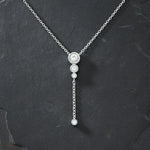 "Silberne Y-Kette mit drei funkelnden Zirkonia-Steinen in Krappenfassung, herunterhängender Kette und einem weiteren Zirkonia-Stein am Ende, präsentiert auf dunklem, kontrastierendem Schieferhintergrund. Elegante Damenhalskette mit Anhänger, perfekt für einen modernen, schlichten Look."