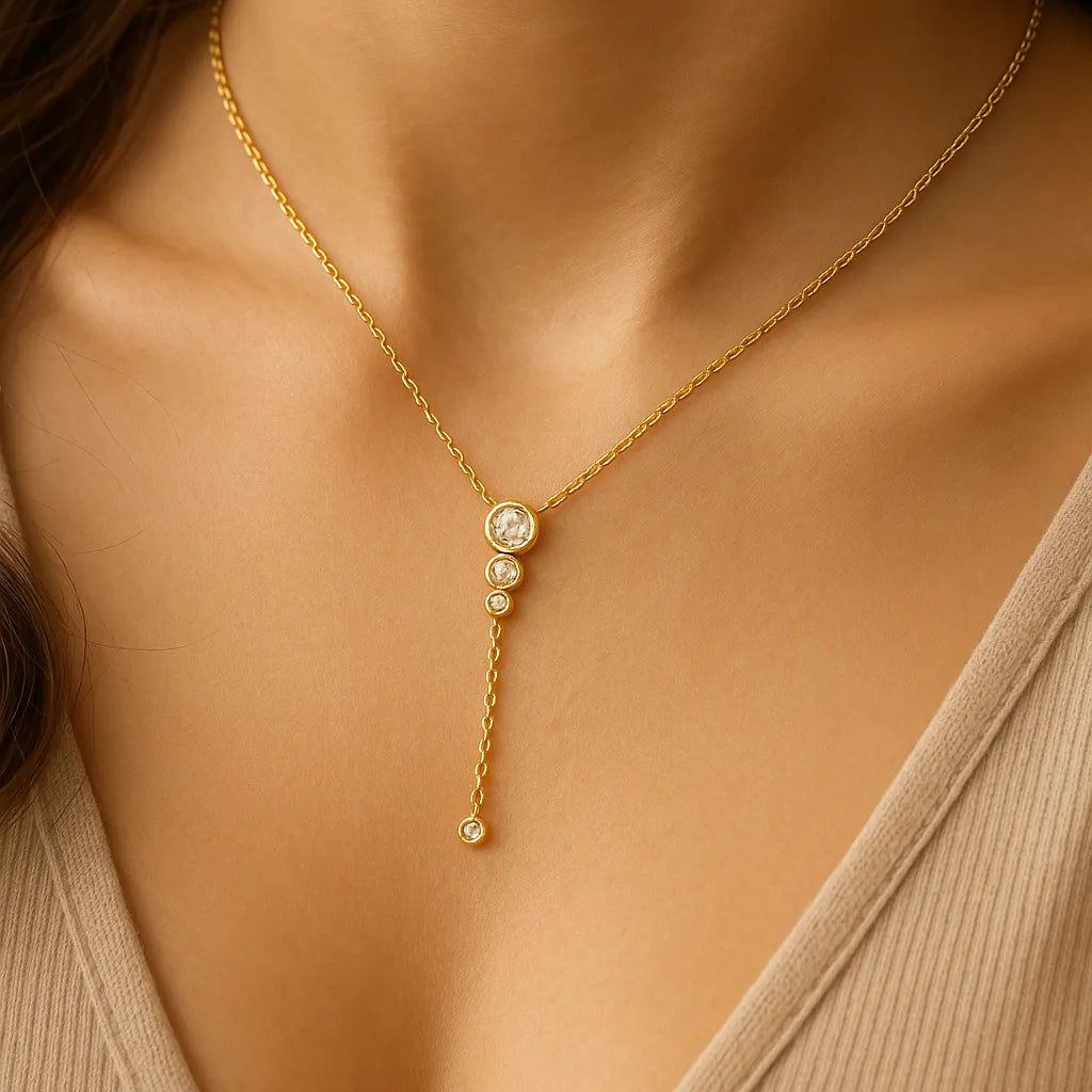 Vergoldete Y-Halskette mit funkelnden Zirkonia-Steinen am Hals einer Frau, eleganter Anhänger mit vier runden Fassungen, femininer Halsschmuck für Alltag und Anlass.
